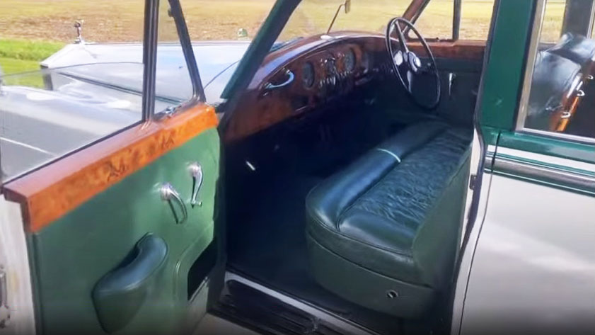 Front passenger seat inside a 1957 Rolls Royce Silver Cloud I with dark green leather upholstery and polished wooden dashboard. Elegant British classic wedding car interior in Littlehampton, West Sussex.