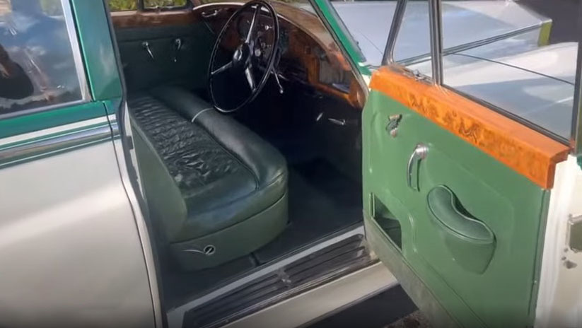 Driver’s seat inside a 1957 Rolls Royce Silver Cloud I featuring dark green leather upholstery, polished wooden dashboard and classic vintage steering wheel. Luxury handcrafted interior of a classic wedding car in West Sussex.
