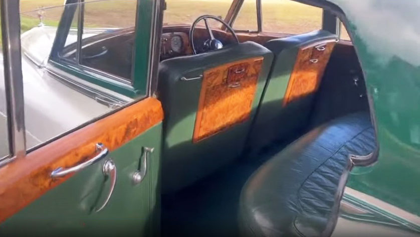 Dark green leather seats and fold down wooden picnic tables inside a 1957 Rolls Royce Silver Cloud I. Handcrafted vintage Rolls Royce interior with luxury wedding car styling in West Sussex.