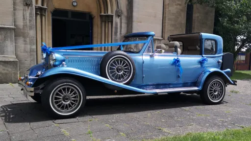 Left side view of a blue vintage Beauford wedding car with open Sedanca roof and cream leather interior at a wedding venue.