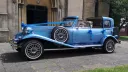 Left side view of a blue vintage Beauford wedding car with open Sedanca roof and cream leather interior at a wedding venue.