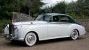 Left side view of a white 1957 Rolls Royce Silver Cloud I with dark green roof in the Sussex countryside. Elegant vintage wedding transport with chrome bumpers and whitewall tyres in West Sussex.