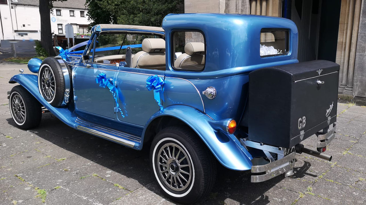 Rear side view of a blue four door Beauford Sedanca wedding car showing vintage body styling and chauffeur driven elegance.