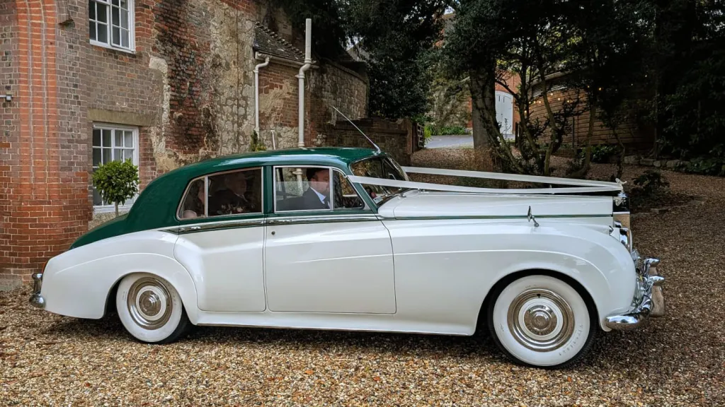 Right side view of a 1957 Rolls Royce Silver Cloud I in white with contrasting dark green roof and matching green leather interior in West Sussex. Luxury classic wedding car photographed outdoors near Littlehampton.