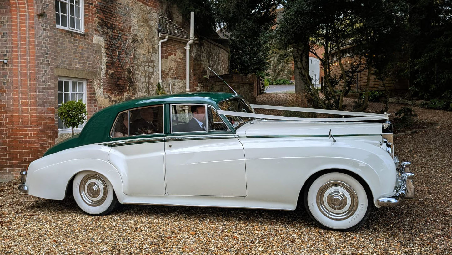 Right side view of a 1957 Rolls Royce Silver Cloud I in white with contrasting dark green roof and matching green leather interior in West Sussex. Luxury classic wedding car photographed outdoors near Littlehampton.