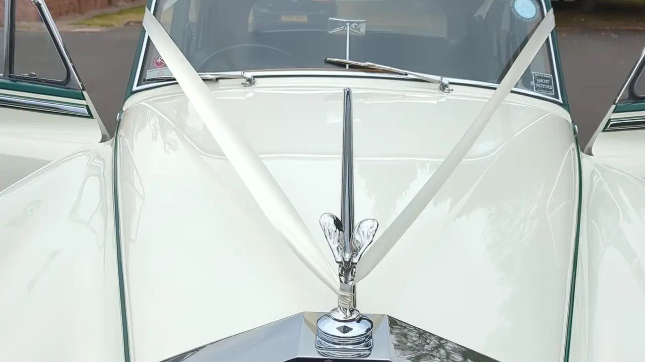 Spirit of Ecstasy bonnet ornament on a 1957 Rolls Royce Silver Cloud I decorated with white wedding ribbons. Close up detail of a classic Rolls Royce wedding car in West Sussex.