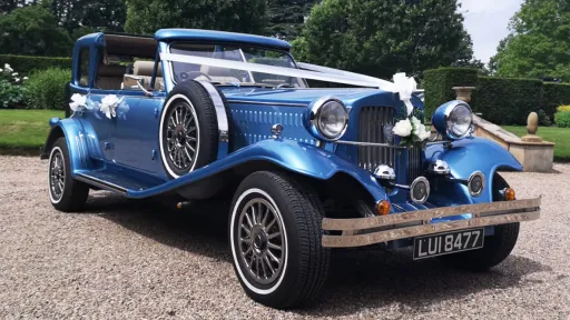 Blue vintage Beauford wedding car decorated with wedding ribbons and bows, photographed outside a countryside wedding venue.