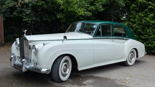 1957 white Rolls Royce Silver Cloud I with dark green roof and whitewall tyres parked in a woodland setting in West Sussex. Elegant vintage chauffeur driven wedding car with timeless styling.