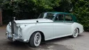 1957 white Rolls Royce Silver Cloud I with dark green roof and whitewall tyres parked in a woodland setting in West Sussex. Elegant vintage chauffeur driven wedding car with timeless styling.