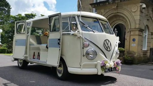 Front three quarter view of a cream and light blue Volkswagen VW Split Screen Campervan wedding vehicle decorated with pink flowers and ribbons, parked outside a church in Southport, Lancashire.