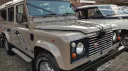 Close-up front side view of beige Land Rover Defender with chrome side steps and classic grille.