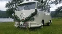 Front view of a cream Volkswagen VW Split Screen Campervan wedding hire vehicle parked beside a lake in Lancashire, decorated with greenery and floral arrangements on the front bumper.
