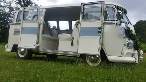 Classic cream and light blue Volkswagen VW Split Screen Campervan with its rear double doors open, showing the spacious striped leather seating and retro interior styling, photographed on grass in Lancashire.