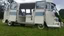 Classic cream and light blue Volkswagen VW Split Screen Campervan with its rear double doors open, showing the spacious striped leather seating and retro interior styling, photographed on grass in Lancashire.