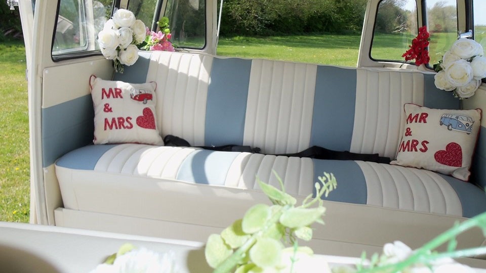 Interior of a classic Volkswagen VW Split Screen Campervan featuring forward facing striped cream and blue leather bench seating with personalised Mr & Mrs wedding cushions and floral décor.