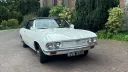 Front angle view of a classic white Chevrolet Corvair Convertible wedding car with chrome detailing and convertible roof folded down, parked at a wedding venue in Lancashire.