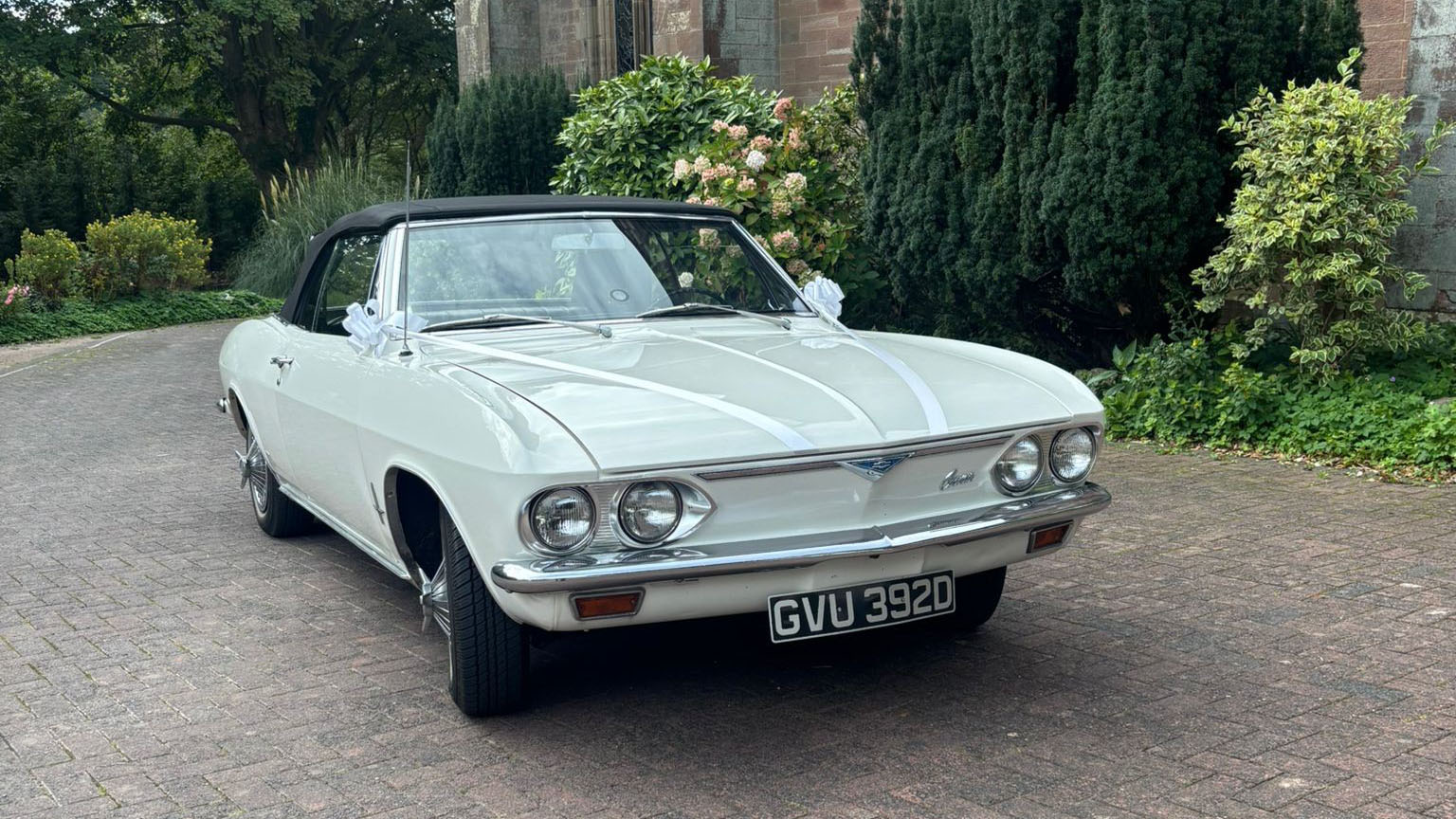 Front angle view of a classic white Chevrolet Corvair Convertible wedding car with chrome detailing and convertible roof folded down, parked at a wedding venue in Lancashire.