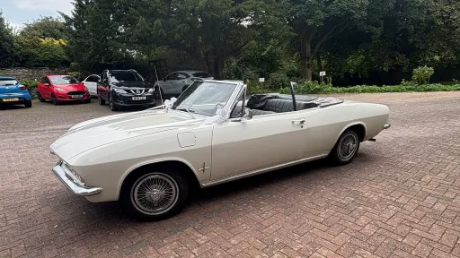Classic white Chevrolet Corvair Convertible photographed from the side with the roof down, showing its long vintage American styling and chrome trim details.