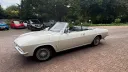 Classic white Chevrolet Corvair Convertible photographed from the side with the roof down, showing its long vintage American styling and chrome trim details.