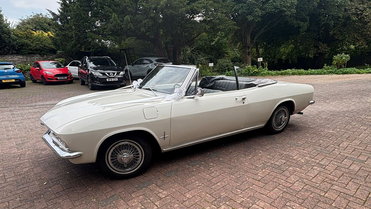 Classic white Chevrolet Corvair Convertible photographed from the side with the roof down, showing its long vintage American styling and chrome trim details.