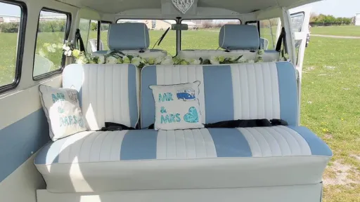 Rear facing striped cream and light blue leather bench seating inside a Volkswagen VW Split Screen Campervan wedding car, complete with personalised wedding cushions and countryside backdrop.