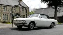Classic white Chevrolet Corvair Convertible with the black convertible roof raised, parked outside a stone wedding venue in Lancashire.