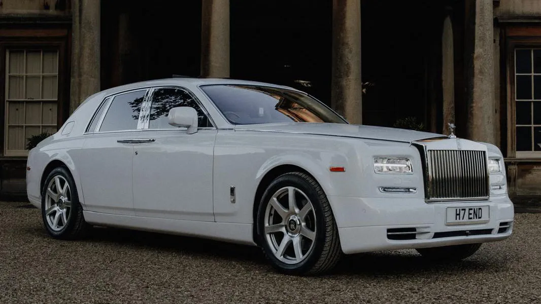 Side view of a white Rolls-Royce Phantom parked in fron of a venue