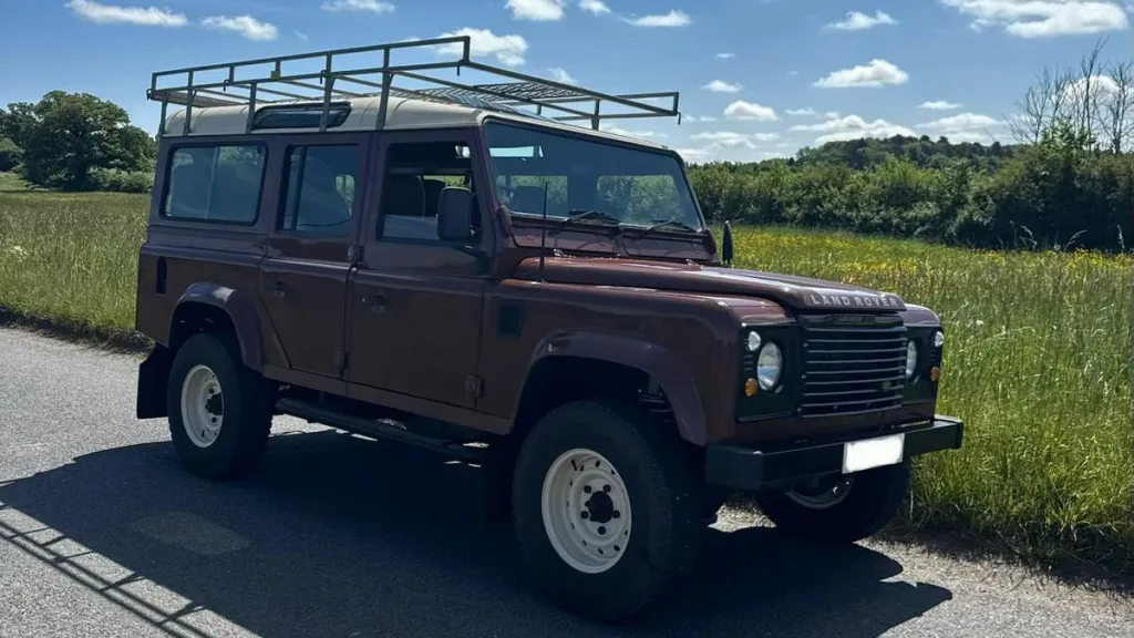 Front side view of brown Land Rover Defender wedding car parked in countryside setting under blue skies.
