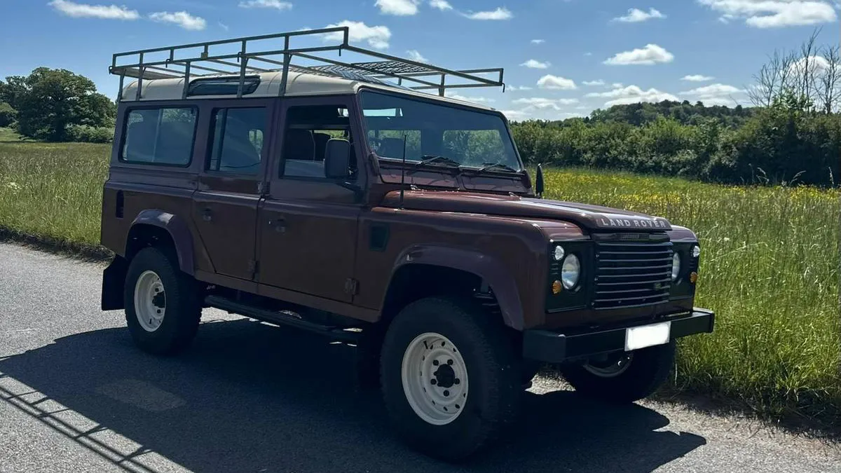 Front side view of brown Land Rover Defender wedding car parked in countryside setting under blue skies.
