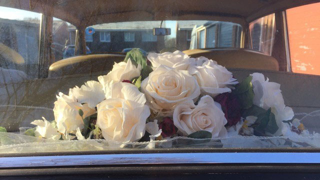 Cream silk wedding flowers displayed on the rear parcel shelf of a Rolls-Royce Silver Shadow.