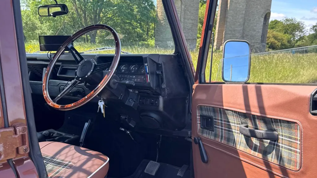 Driver's seat and dashboard inside classic Land Rover Defender with traditional controls and steering wheel.