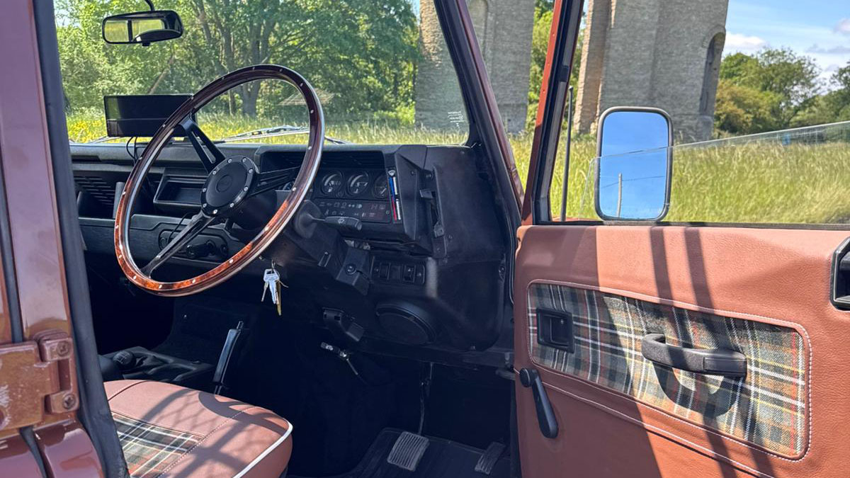 Driver's seat and dashboard inside classic Land Rover Defender with traditional controls and steering wheel.