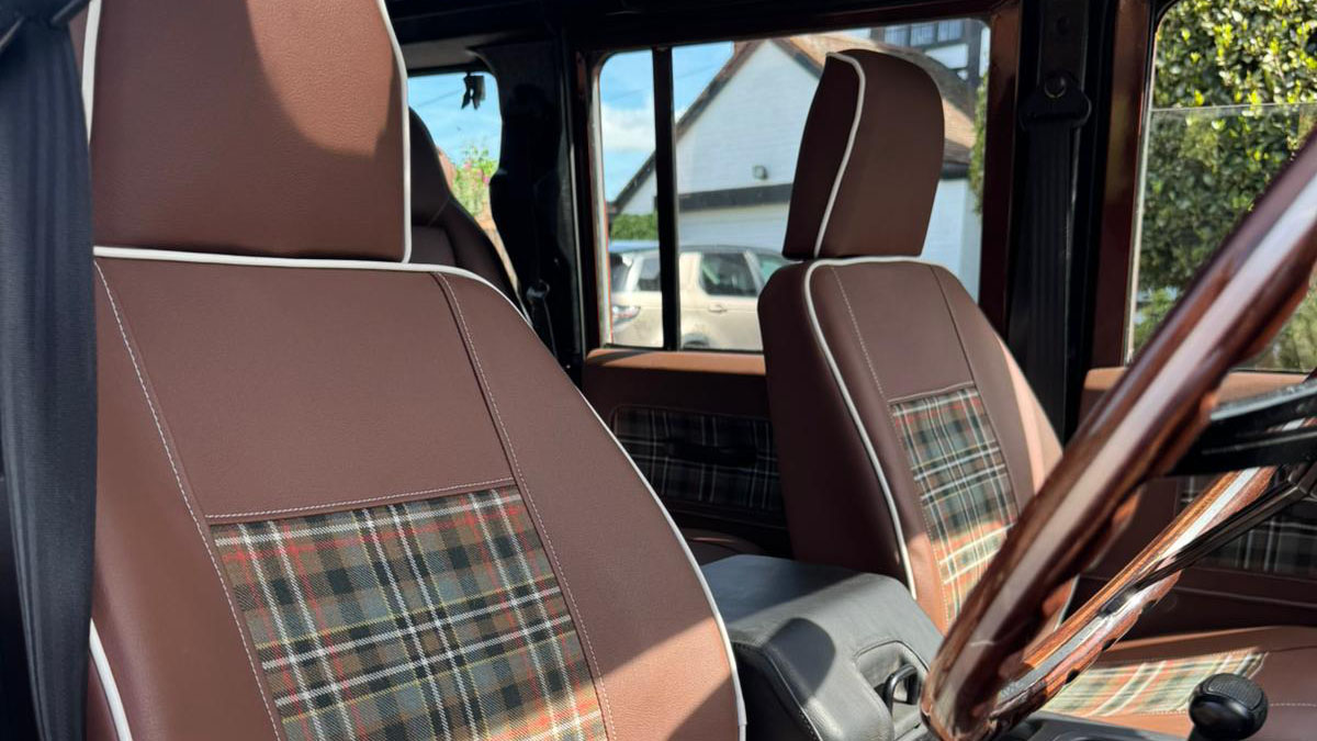 Front interior seating inside Land Rover Defender with brown upholstery and tartan seat inserts.
