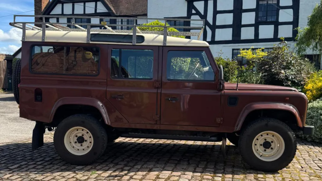 Full right side profile of classic brown Land Rover Defender parked outside wedding venue.