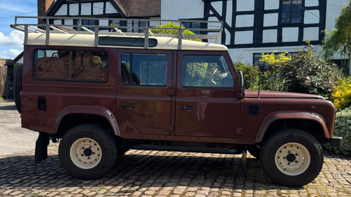 Full right side profile of classic brown Land Rover Defender parked outside wedding venue.
