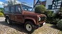 Brown Land Rover Defender wedding car parked outside countryside church venue.