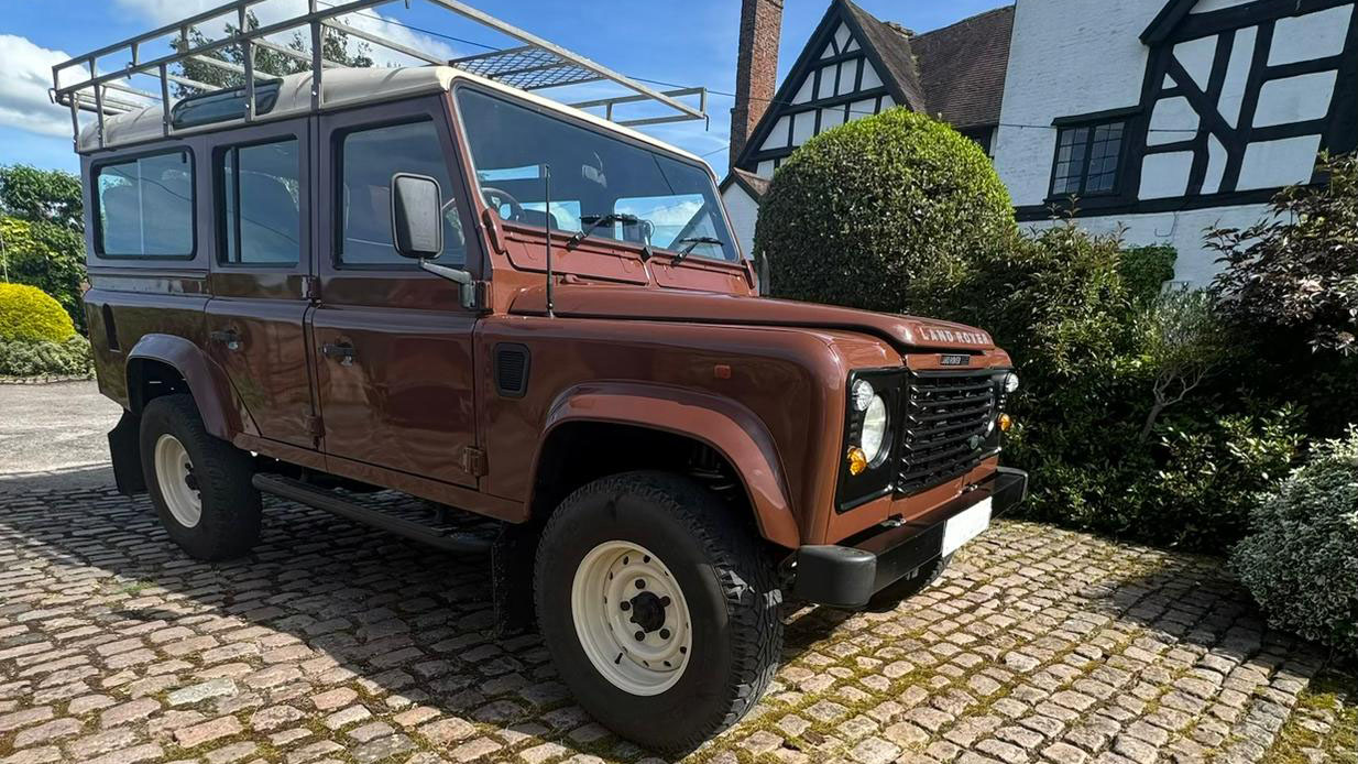 Brown Land Rover Defender wedding car parked outside countryside church venue.
