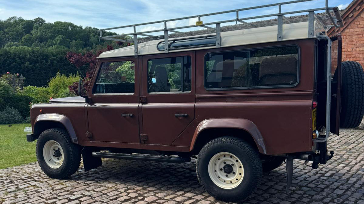 Full left side profile of brown Land Rover Defender wedding vehicle with long wheelbase body.