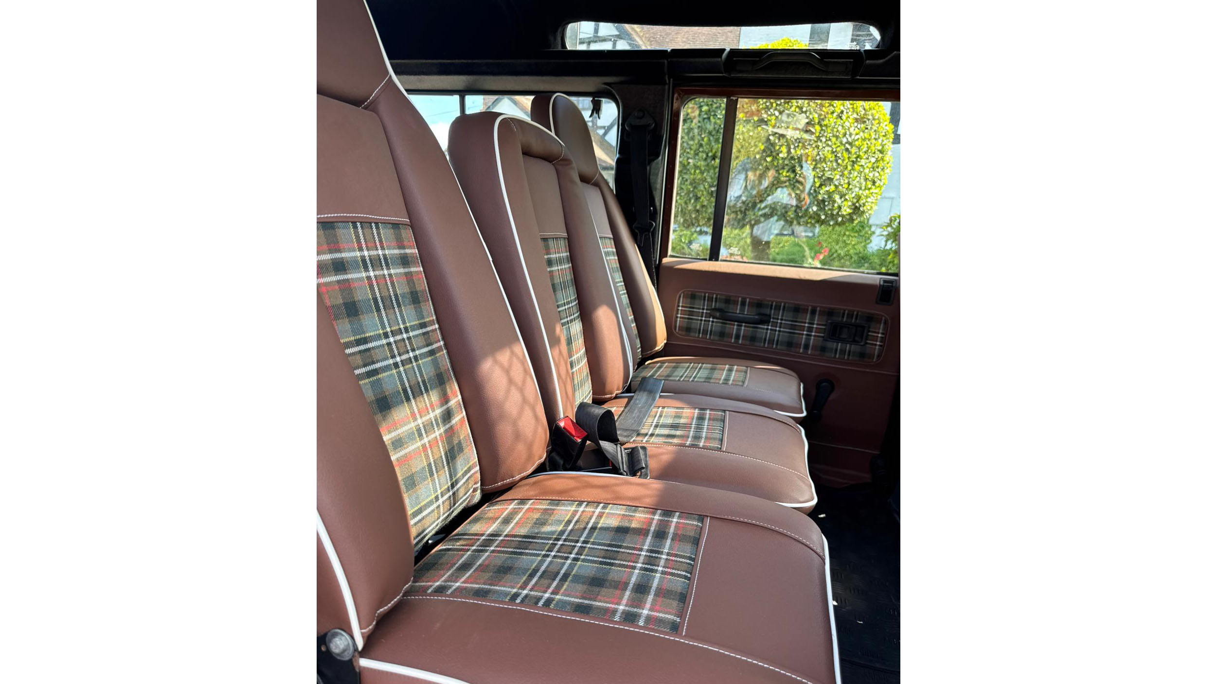 Forward facing rear passenger seats inside Land Rover Defender with brown and tartan upholstery.