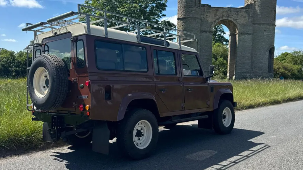 Rear view of classic brown Land Rover Defender wedding car with roof rack and rear mounted spare wheel.