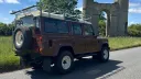 Rear view of classic brown Land Rover Defender wedding car with roof rack and rear mounted spare wheel.