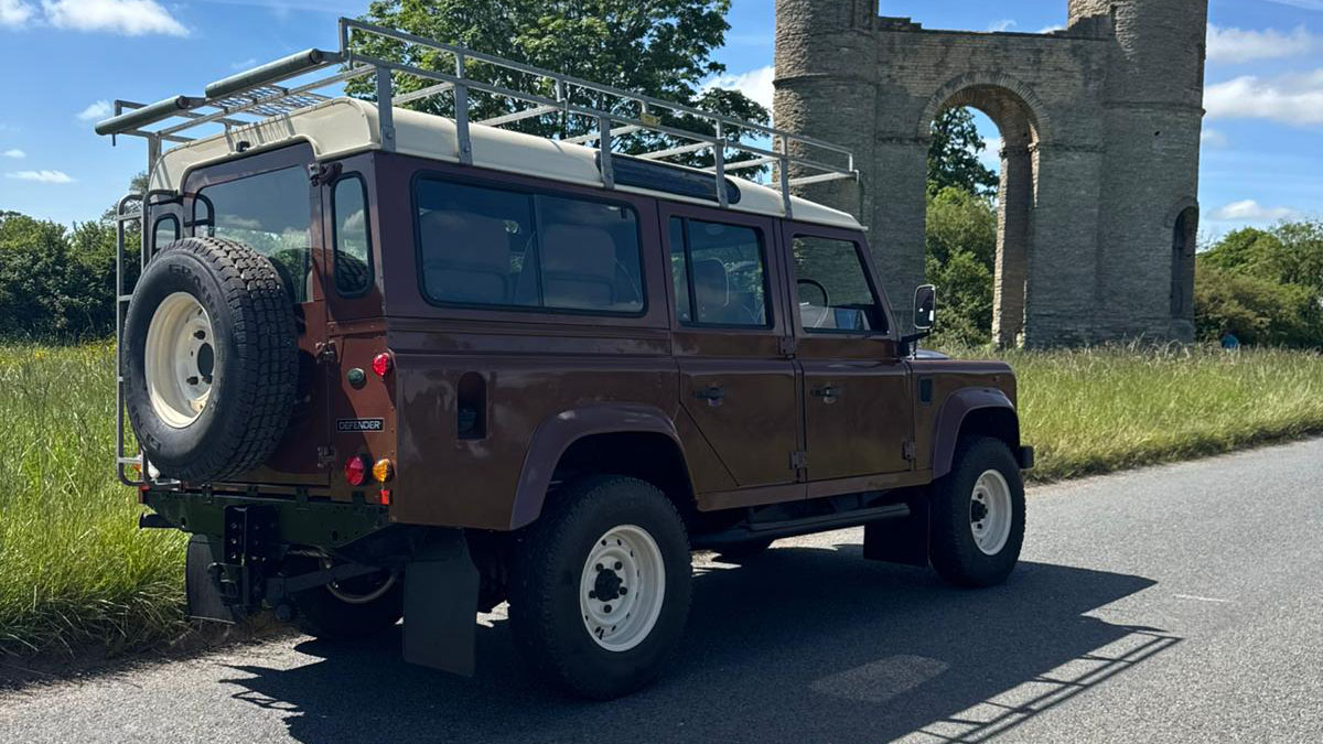 Rear view of classic brown Land Rover Defender wedding car with roof rack and rear mounted spare wheel.