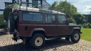 Right side view of brown Land Rover Defender wedding car with roof rack and countryside backdrop.