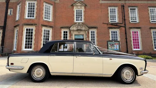 Right side view of a black and ivory 1970 Rolls-Royce Silver Shadow Mark 1 wedding car outside a brick building.