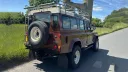 Rear angle view of brown Land Rover Defender showing spare wheel carrier and roof rack.
