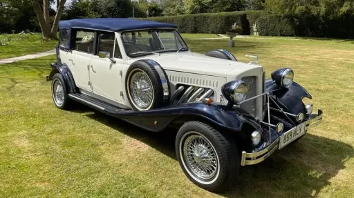 Blue and ivory Beauford wedding car with soft top roof parked at countryside venue.