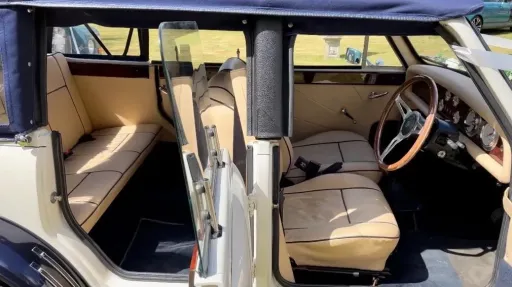 Open door view inside vintage Beauford convertible showing cream leather seating and classic dashboard.