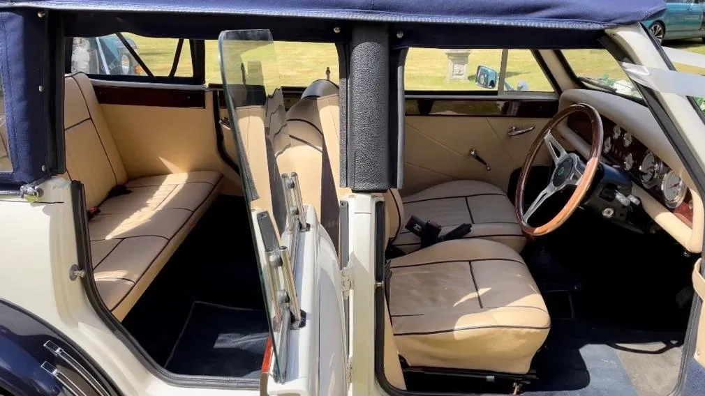 Open door view inside vintage Beauford convertible showing cream leather seating and classic dashboard.