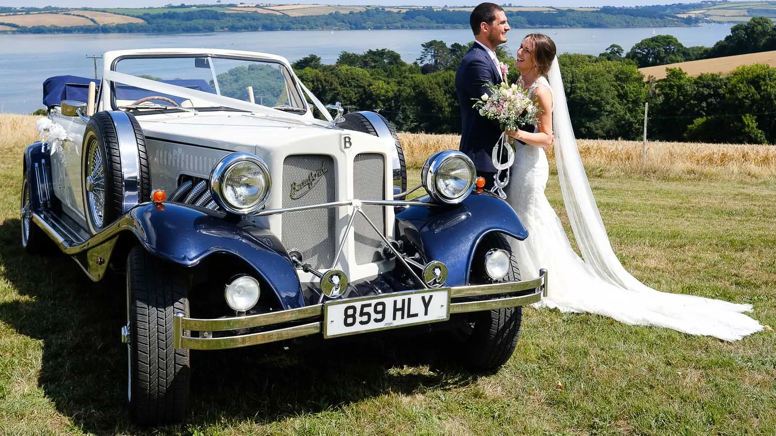 Bride and groom beside vintage Beauford convertible wedding car in Kent countryside.