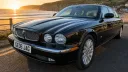 Black Jaguar stretch limousine parked beside coastline with luxury chrome grille and cream interior.